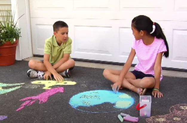 Children playing, using sidewalk chalk on a driveway.